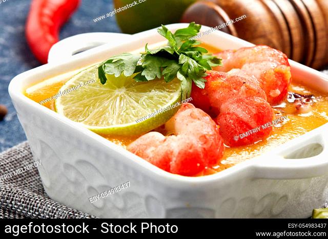 Delicious fish cream soup with shrimps in white bowl served with spices, lime and pieces of bread on dark blue marble background. Healthy food