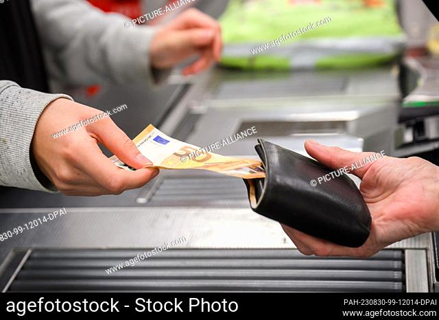 30 August 2023, Lower Saxony, Hanover: A cashier removes a 50-euro bill from a customer's purse at a supermarket checkout