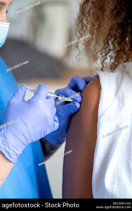 Female nurse injecting COVID-19 vaccine in patient's arm at hospital