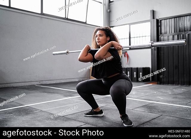 Curly haired young woman practicing squats in gym