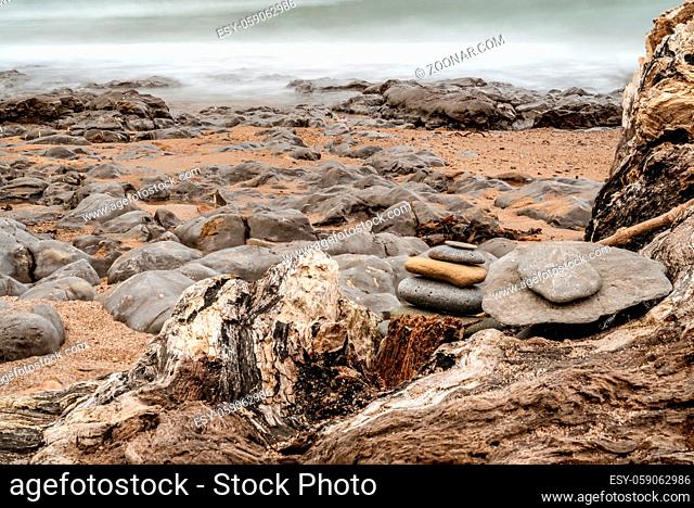 A stone pile on a tree trunk on a stony beach, seen at Cocklawburn Beach near Berwick-upon-Tweed in Northumberland, England, UK