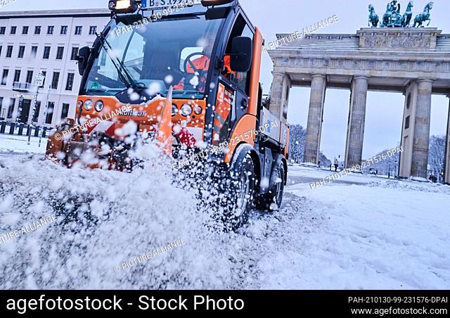 30 January 2021, Berlin: Snow sprays into the air as a BSR snow plough drives past the Brandenburg Gate. Last night it snowed in Berlin