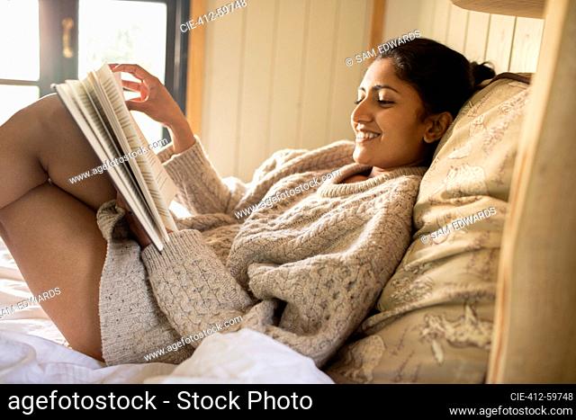Carefree young woman reading book in bed