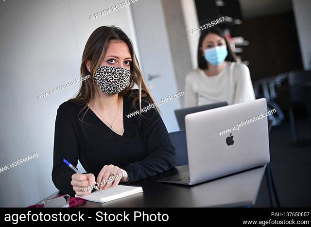 Themed picture CoWorking Space. Two young women sit at individual tables and wear face masks and masks. You are working on your laptop in a CoWorking office on...