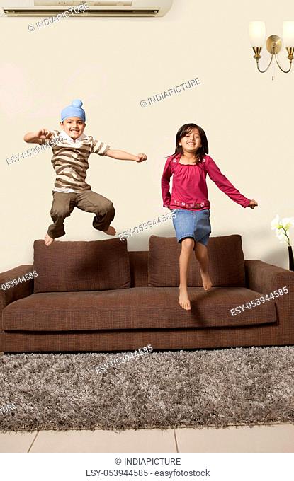 Happy brother and sister jumping on sofa at home