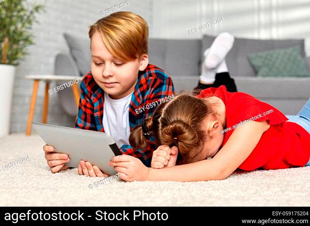 happy brother and sister with tablet lying on floor. Children use gadgets at home