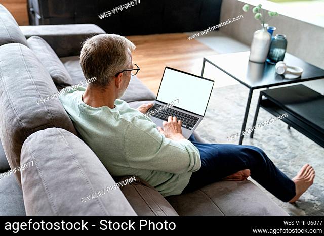 Businessman using laptop on sofa in living room at home