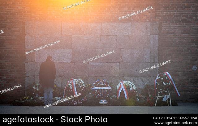 24 January 2020, Poland, Oswiecim: Early in the morning, a man lays flowers on the Black Wall in the courtyard between Blocks 10 and 11 of the former Auschwitz...