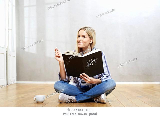 Portrait of smiling blond woman with book sitting on the floor