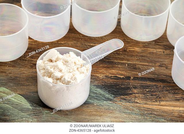 scoop of whey protein powder on a wooden surface surrounded by empty plastic scoops