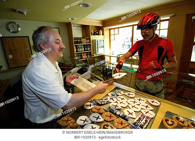 A cyclist purchasing pastries shaped like a mitre, in honor of Pope Benedict XVI, Marktl am Inn, 'Little Market on the Inn River', Chiemgau, Bavaria, Germany