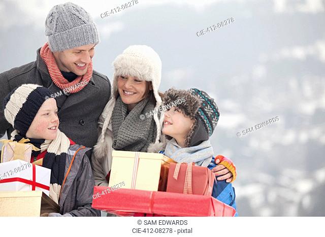 Happy family carrying Christmas gifts in snow