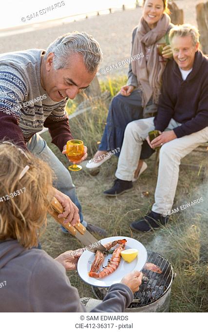 Mature couples barbecuing and drinking wine on beach