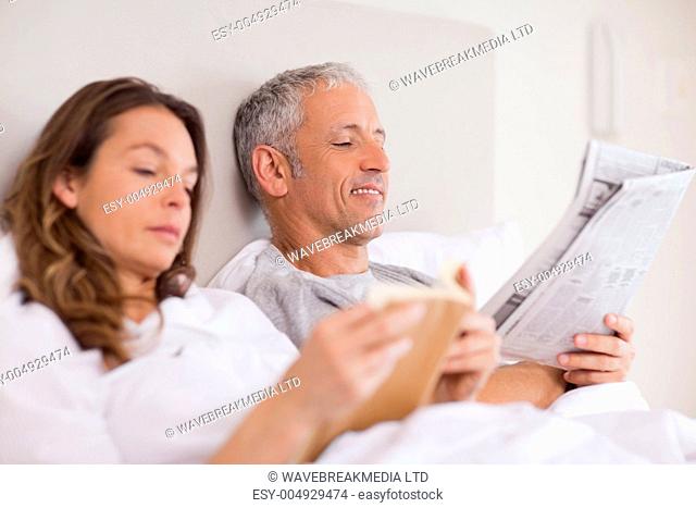 Happy woman reading a book while her husband is reading a newspaper
