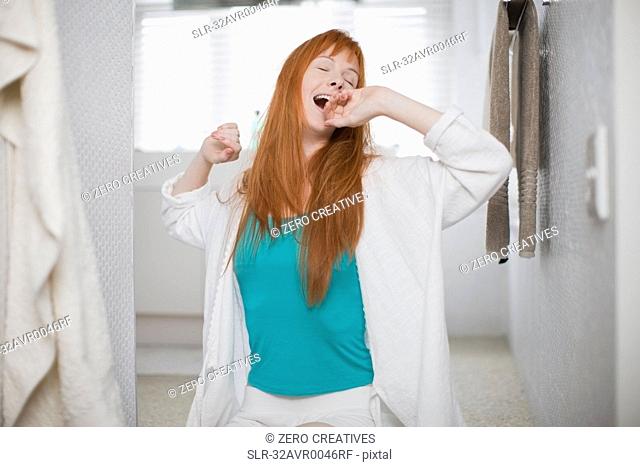 Woman in bathrobe yawning and stretching