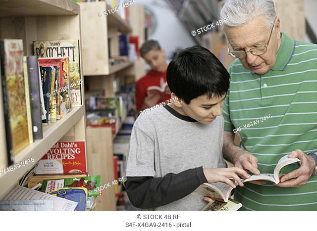 Grandfather and boy reading a book in front of a bookshelf, fully-released