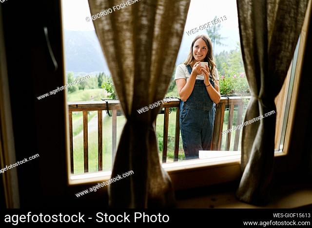 Happy woman standing with coffee cup on balcony