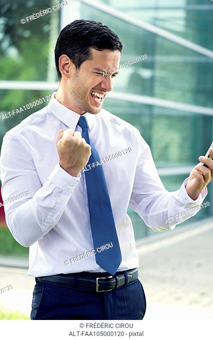 Businessman looking at cell phone and making victorious gesture