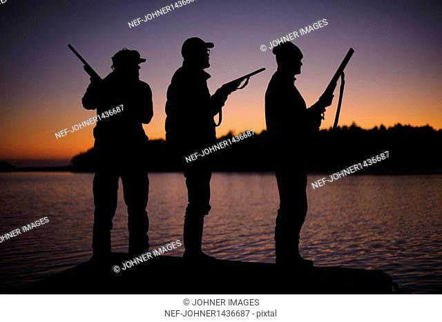 Silhouette of three hunters on jetty at sunset