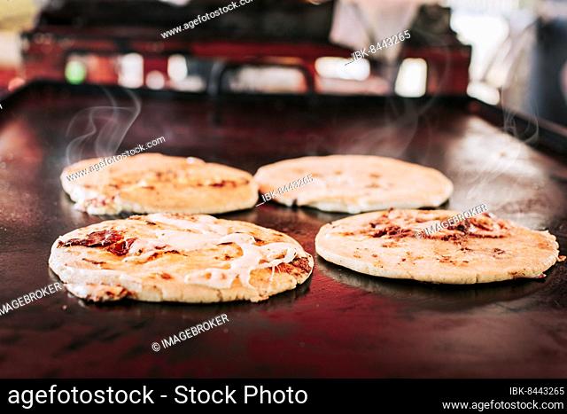 Traditional Salvadoran pupusas with melted cheese on a grill, Traditional cheese pupusas on the grill. Side view of four traditional crispy pupusas on the grill