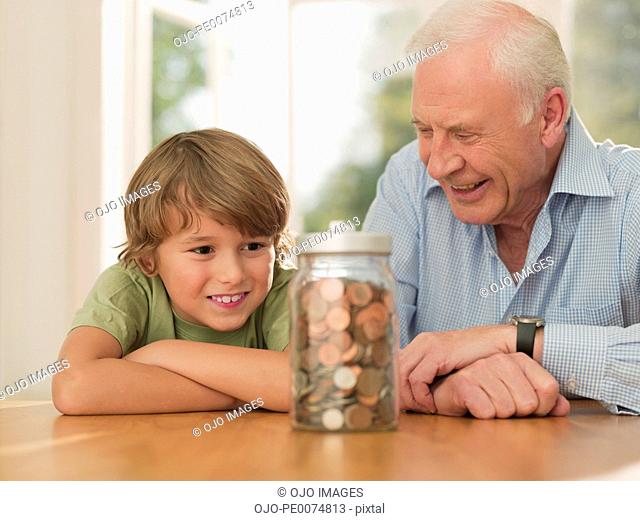Grandfather and grandson looking at jar full of coins