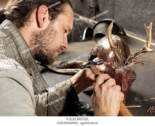 Blacksmith hammering copper on deer sculpture in workshop
