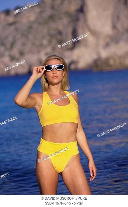 Portrait of a young woman standing on the beach wearing sunglasses