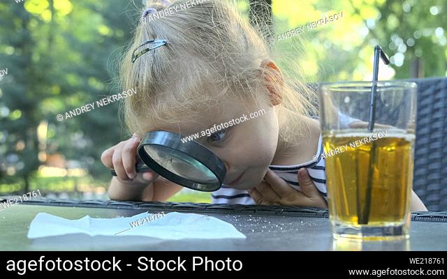 Little girl carefully looks into the lens at the salt. Close-up of blonde girl is studying salt crystals while looking at her through magnifying glass while...