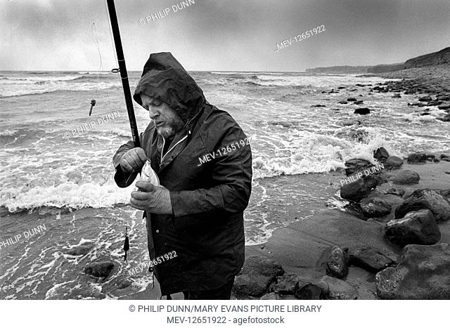 A beach fisherman unhooks a flounder he has just caught with rod and line at Col Huw Bay, Llantwit Major, Glamorgan, South Wales