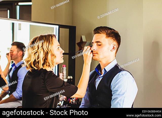 Makeup artist doing professional makeup for young man. Handsome model man in studio