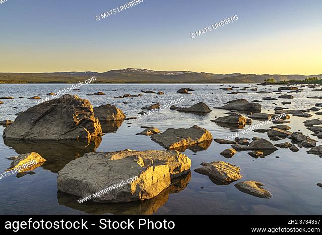 Landscape in evening light with mountains with little snow, clear sky and rocks in the water, Swedish Lapland, Sweden