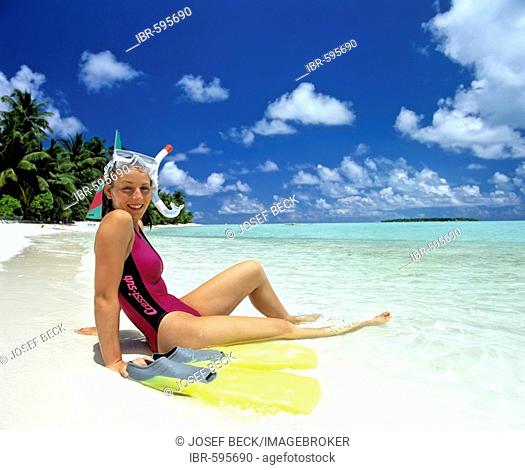 Young woman relaxing on beach with snorkeling gear beside her, island with palm trees, Maldives, Indian Ocean