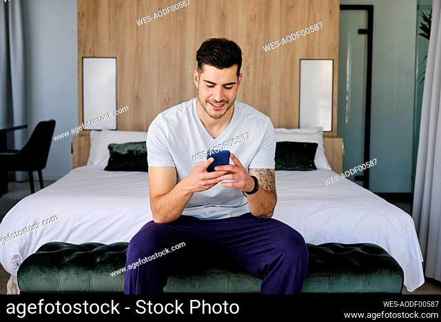 Young man using smart phone in bedroom at home