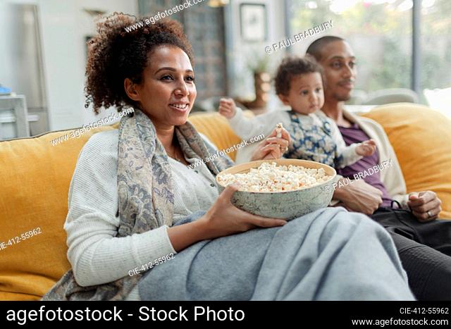Happy family watching movie and eating popcorn on living room sofa