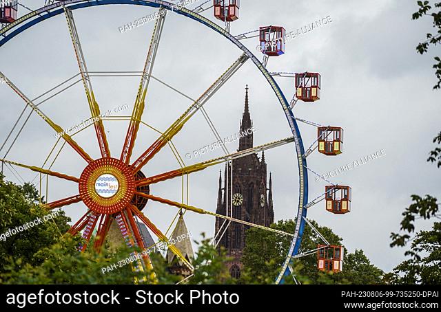 06 August 2023, Hesse, Frankfurt/Main: The sparsely occupied Ferris wheel gondolas stand in front of the cathedral. The Mainfest (04.08.-07.08