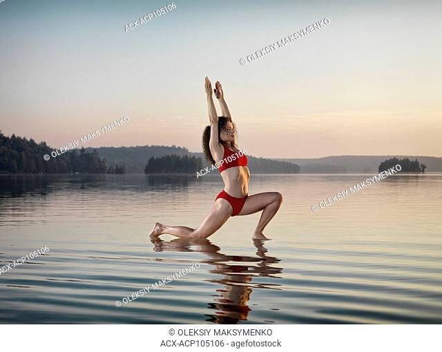 Young woman practicing Hatha yoga Low Lunge on a floating platform in water on the lake during misty sunrise in the morning. Yoga Anjaneyasana posture