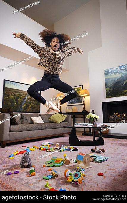 Female ballet dancer and young mother jumping over toys scattered on floor