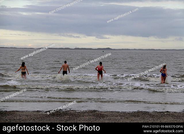 01 January 2021, Lower Saxony, Norderney: With an air and water temperature around five degrees, four people go swimming in the North Sea on the island's...