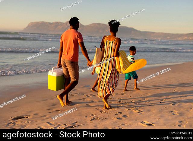 Rear view of african american young couple carrying blankets and cooler at beach againt clear sky