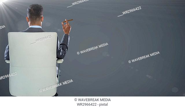 Back of seated business man smoking cigar against grey background with flare