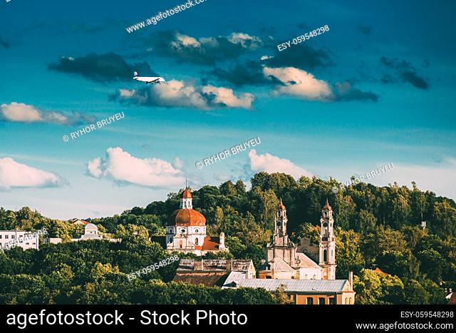 Vilnius, Lithuania. Plane Flying Over Church Of The Ascension And Church Of The Sacred Heart Of Jesus Among Green Foliage. Destination Scenic