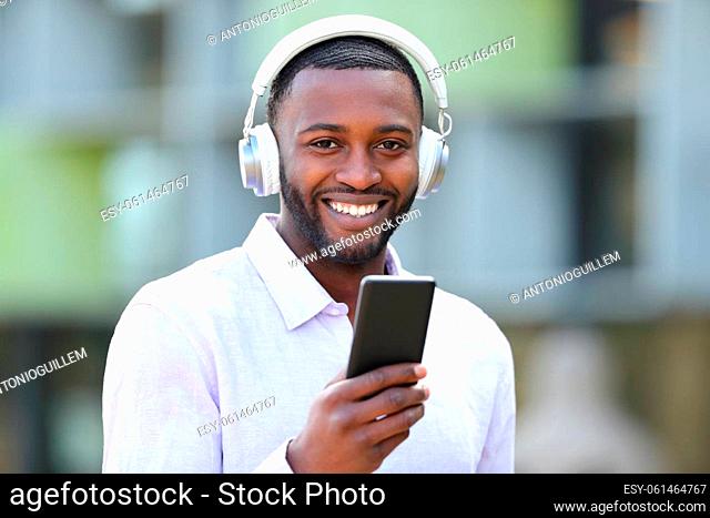 Happy black man listening to music looks at you in the street