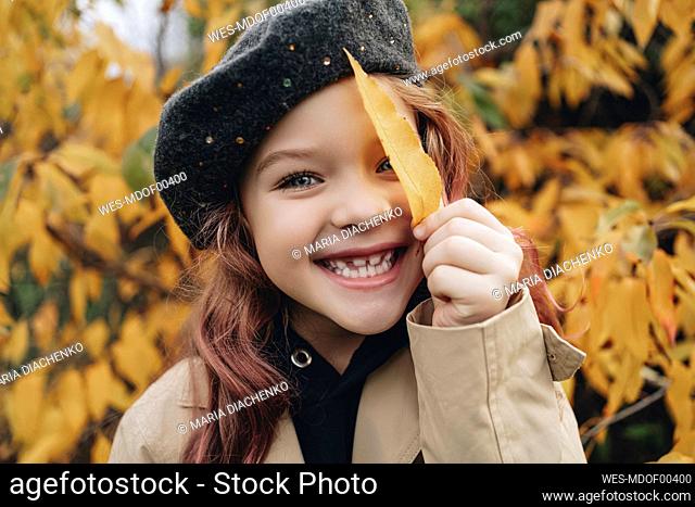 Happy girl playing with yellow leaf in park