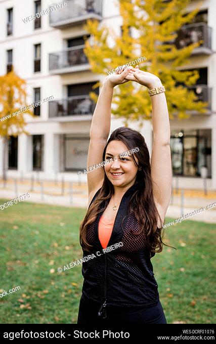 Happy woman with hands raised exercising in public park
