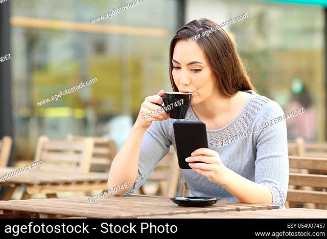 Young woman drinking a cup of coffee checking her smart phone on a coffee shop terrace