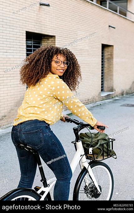 Young woman smiling while standing with bicycle on road