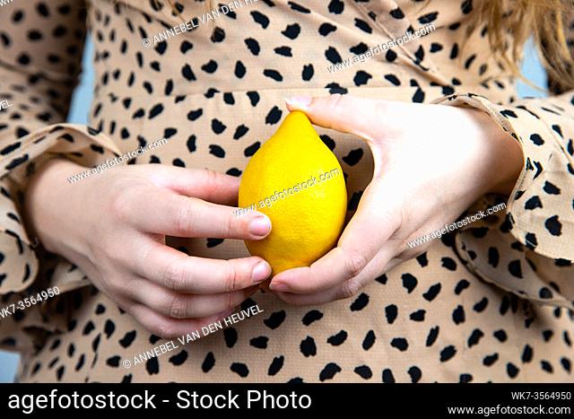 Young beautiful woman holding a fresh yellow lemon in her hands, close-up summer fruit concept healthy