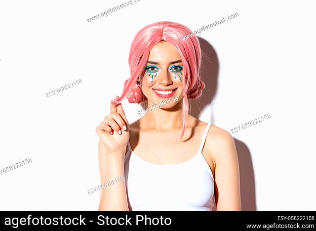 Close-up of beautiful smiling woman in pink wig, celebrating holiday, looking happy at camera, standing over white background