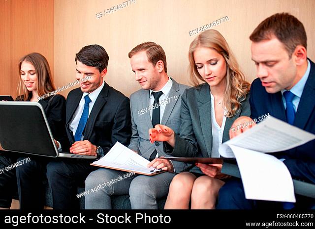Business people working together sitting in a row in lobby and holding laptop and documents on knees