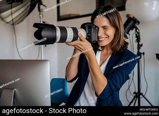 Smiling photographer photographing through digital camera in studio